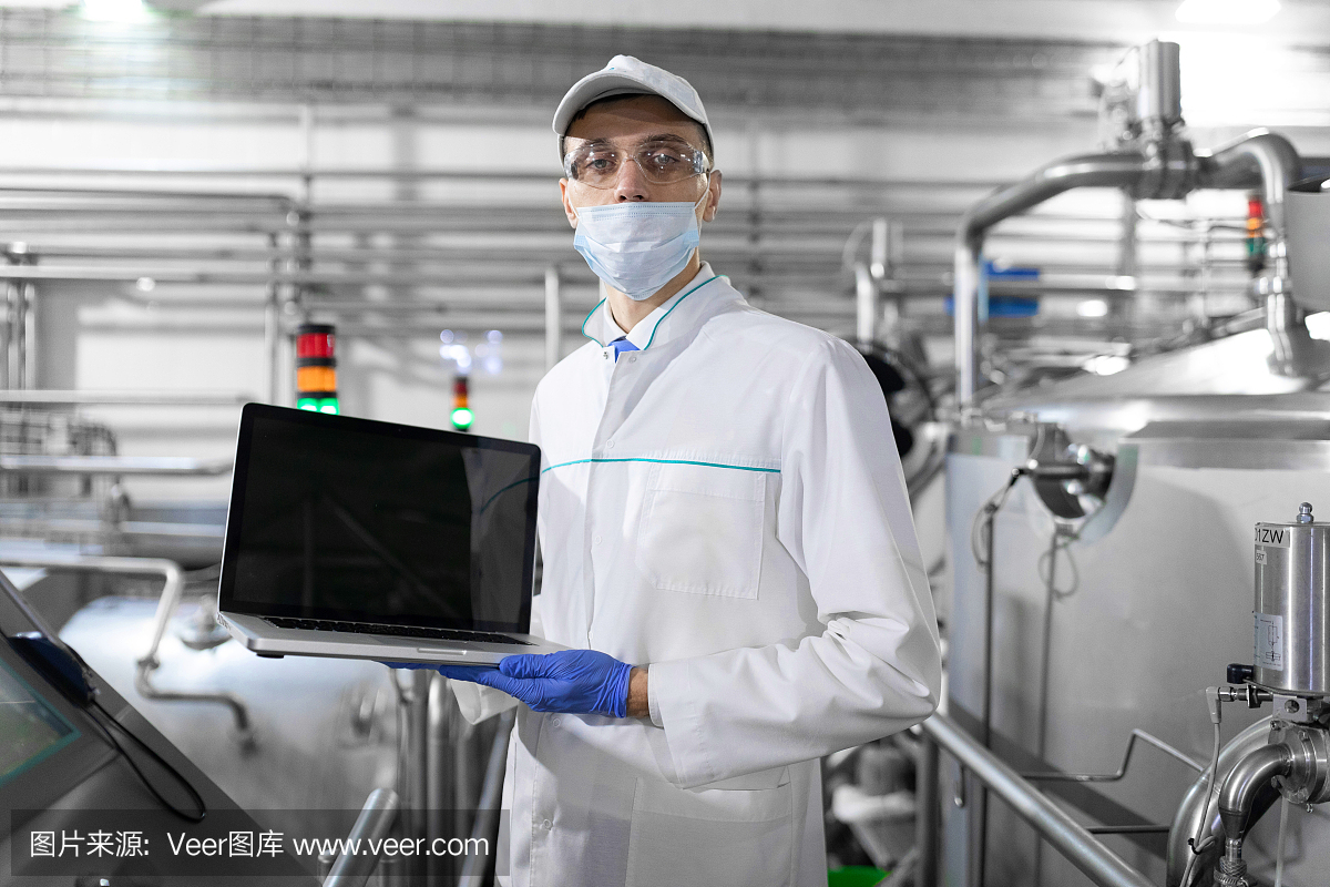一名身穿白色长袍、戴着面具、手里拿着笔记本电脑的男子在工厂里